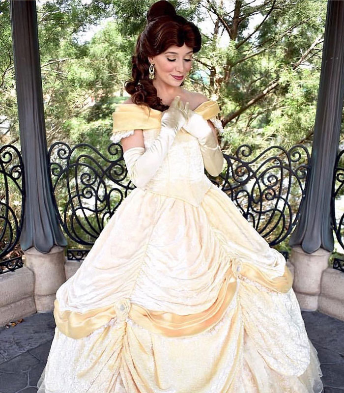 Woman dressed as Belle Disney princess posing by a gazebo outdoors Woman dressed as Belle Disney princess posing by a gazebo outdoors