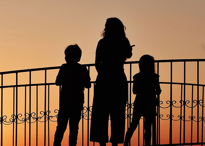 Silhouetted adult and children standing against sunset by balcony