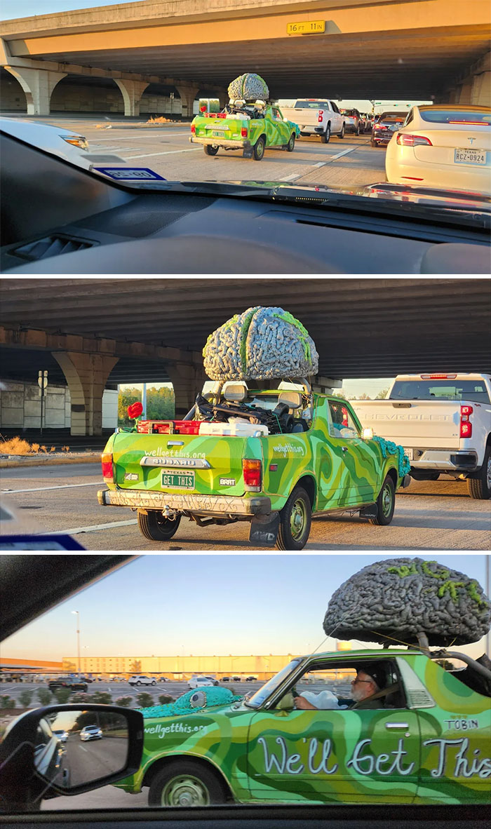 Green pickup with giant brain sculpture on roof driving on highway