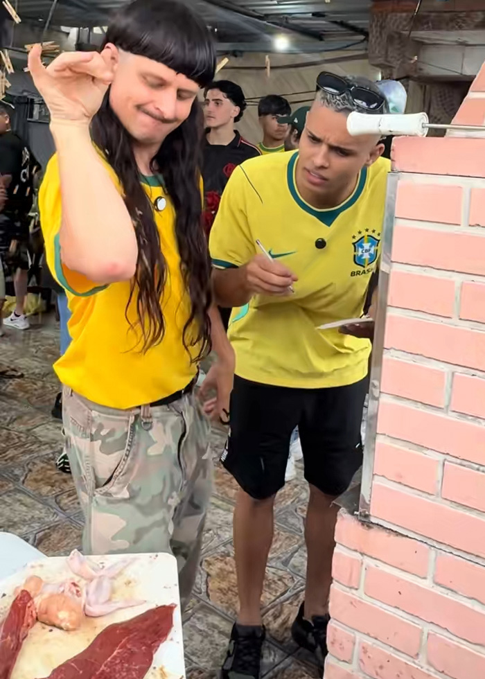 Oliver Tree in Brazil making a gesture while a man in a Brazil soccer shirt writes Oliver Tree in Brazil making a gesture while a man in a Brazil soccer shirt writes