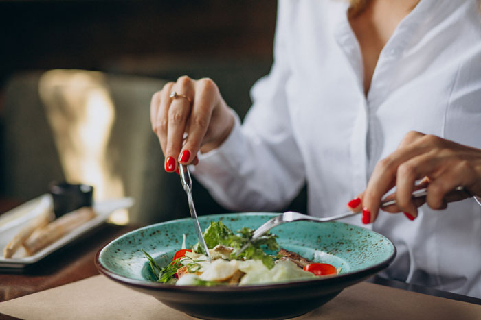 Person cutting salad with fork and knife illustrating Karen dining