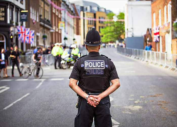 A police officer stands in the street with Union Jack flags, signifying the arrest of a millionaire connected to UK royals. A police officer stands in the street with Union Jack flags, signifying the arrest of a millionaire connected to UK royals.