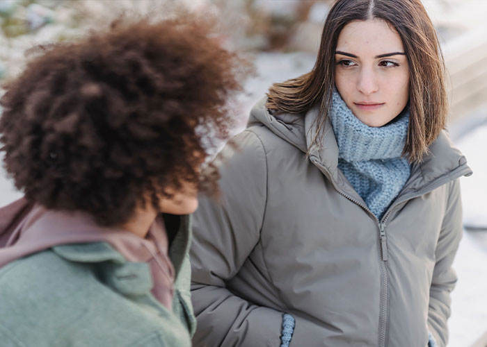 Two friends in winter clothes, one looking away, discussing horrible things committed by close friends that broke people's trust.