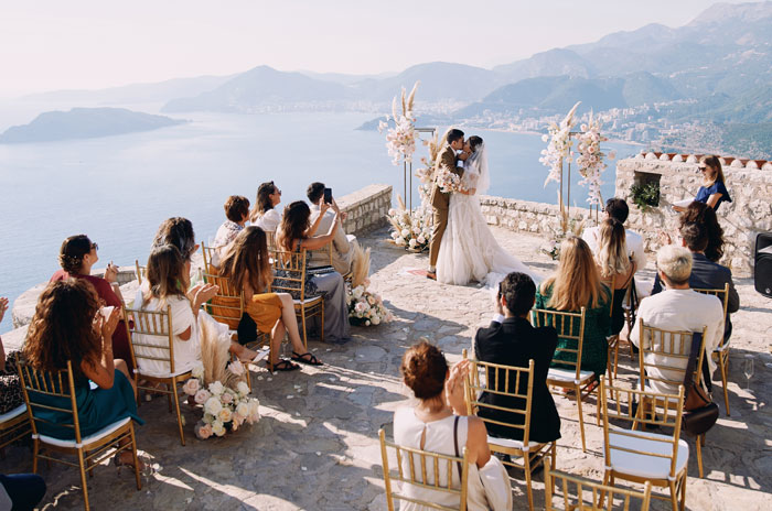 Wedding ceremony with bride and groom kissing outdoors by the sea with guests seated Wedding ceremony with bride and groom kissing outdoors by the sea with guests seated