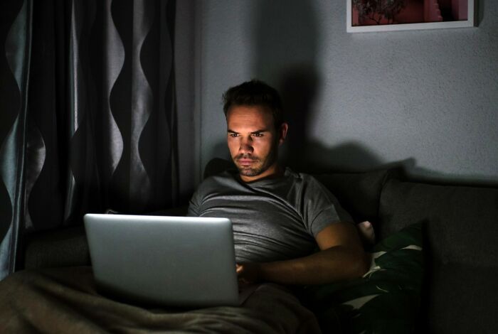 Man using laptop at night with unsettling expression on face