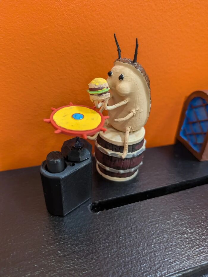 A bizarre insectoid creature holding a tiny burger, sitting on a barrel next to a miniature DJ setup.