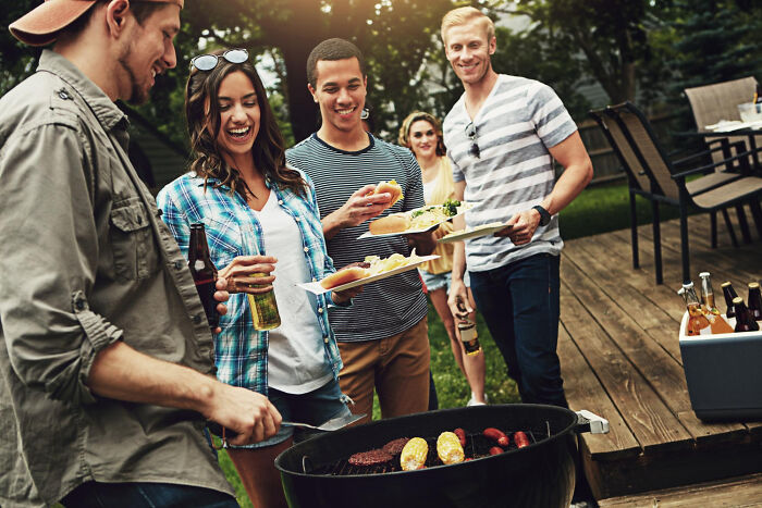 Friends enjoying a backyard BBQ, some holding plates of food, representing disturbing things people learn about friends.