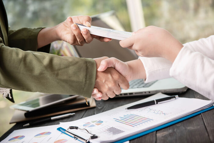 Businesspeople shaking hands and exchanging documents during meeting
