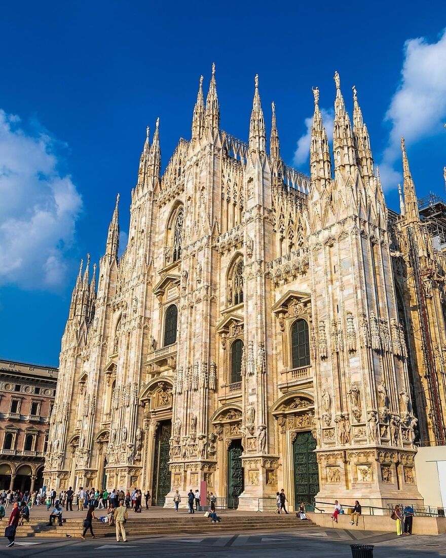 Milan Cathedral facade under bright blue sky with detailed spires and stonework