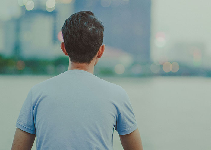 Man in blue shirt looking over blurry cityscape by the water