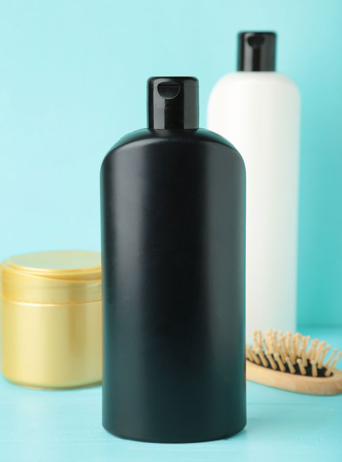 Black shampoo bottle with other hair products and brush on blue background