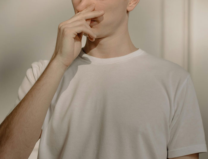 Man in white t-shirt covering nose, indicating bad odor or gross smell