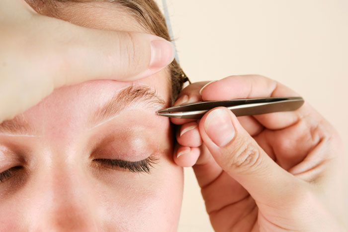Person shaping eyebrows with tweezers to improve appearance