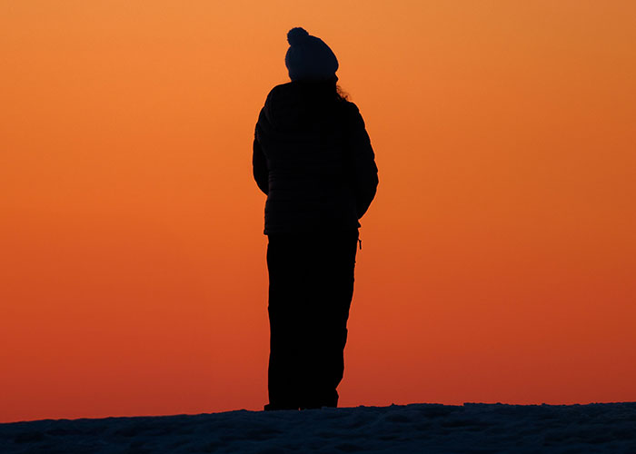 A silhouette of a person standing against an orange sunset, embodying moments when kids cant keep contact with parents.
