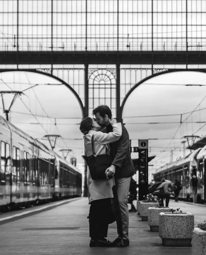 A black and white image of two strangers kissing at a train station, capturing the "Like A Painting" photo trend.