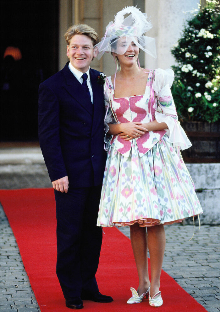 Emma Thompson in a colorful patterned wedding dress with a unique hat, next to Kenneth Branagh.