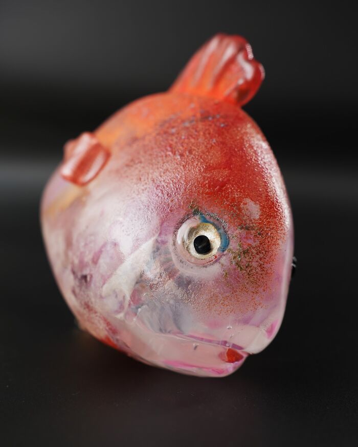 A close-up of a hyper-realistic glass food fish with red and orange hues on a dark background.