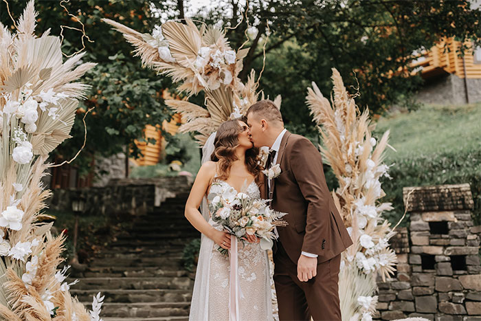 Bride and groom kissing at outdoor wedding ceremony with floral decorations