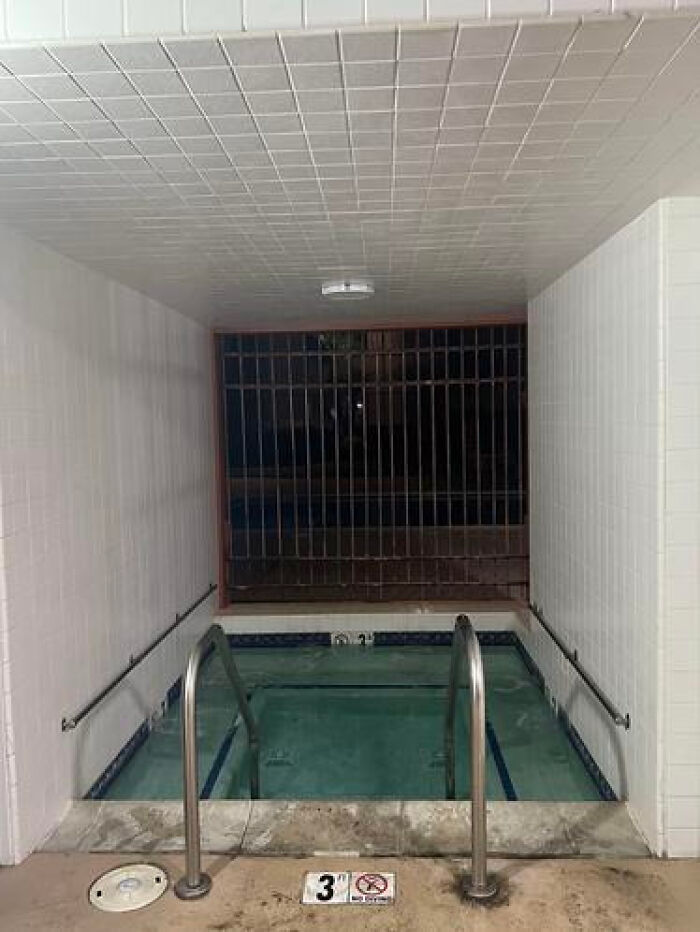 A small, dimly lit swimming pool area with a metal gate, creating a haunting liminal space.