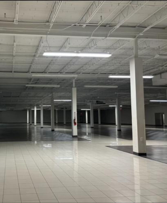 An empty, brightly lit retail space with white tiled floors and exposed ceiling, representing a haunting liminal space.