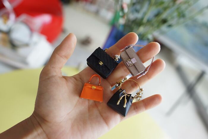 Miniature paper figures of designer handbags held in a person's palm, showing immense detail.
