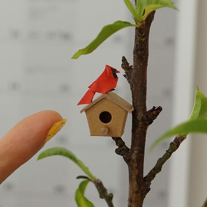 Miniature paper figure of a red cardinal perched on a birdhouse on a branch, showing immense detail.