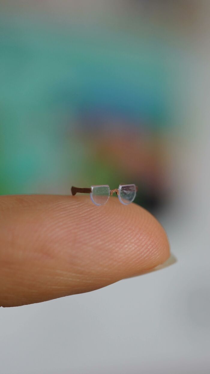 A pair of miniature paper figures of eyeglasses resting on a fingertip, showing immense detail.