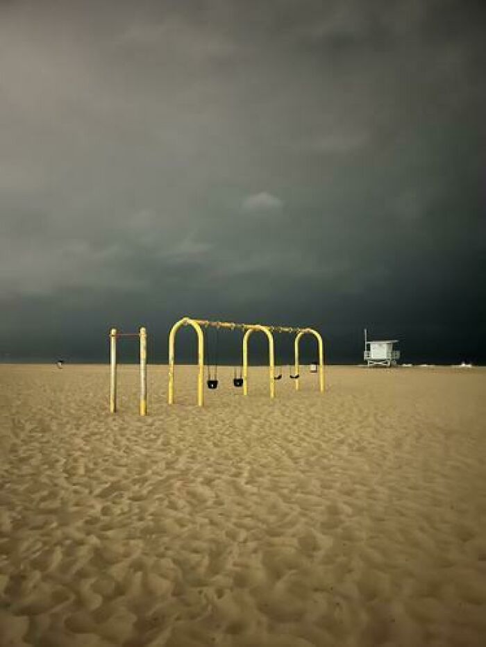 Deserted beach with a yellow swing set and dark, stormy sky, a haunting liminal space.