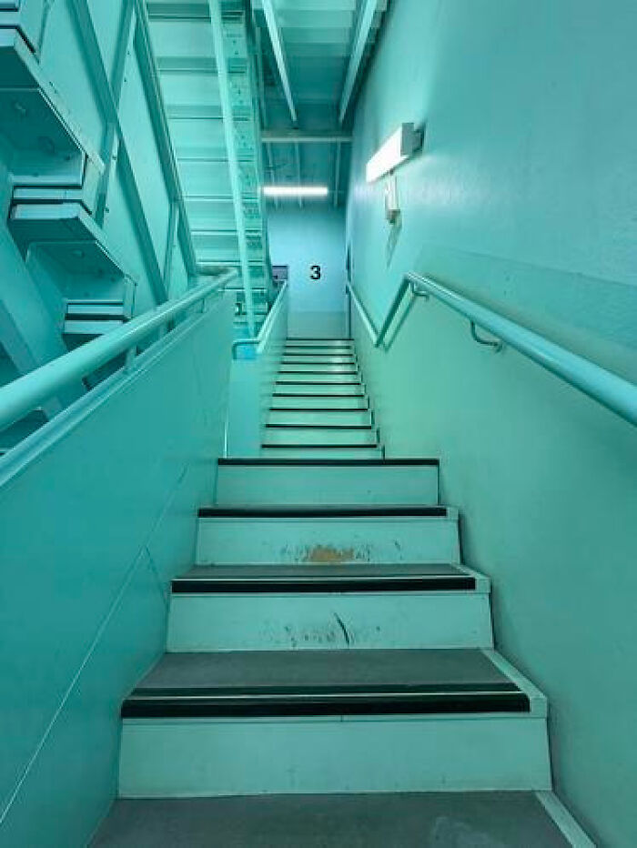 A sterile, light blue stairwell stretching upwards, illustrating a haunting liminal space.