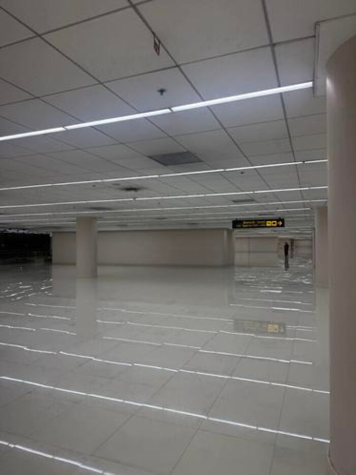 A vast, empty hallway with a shiny floor and distant figures, embodying a haunting liminal space.