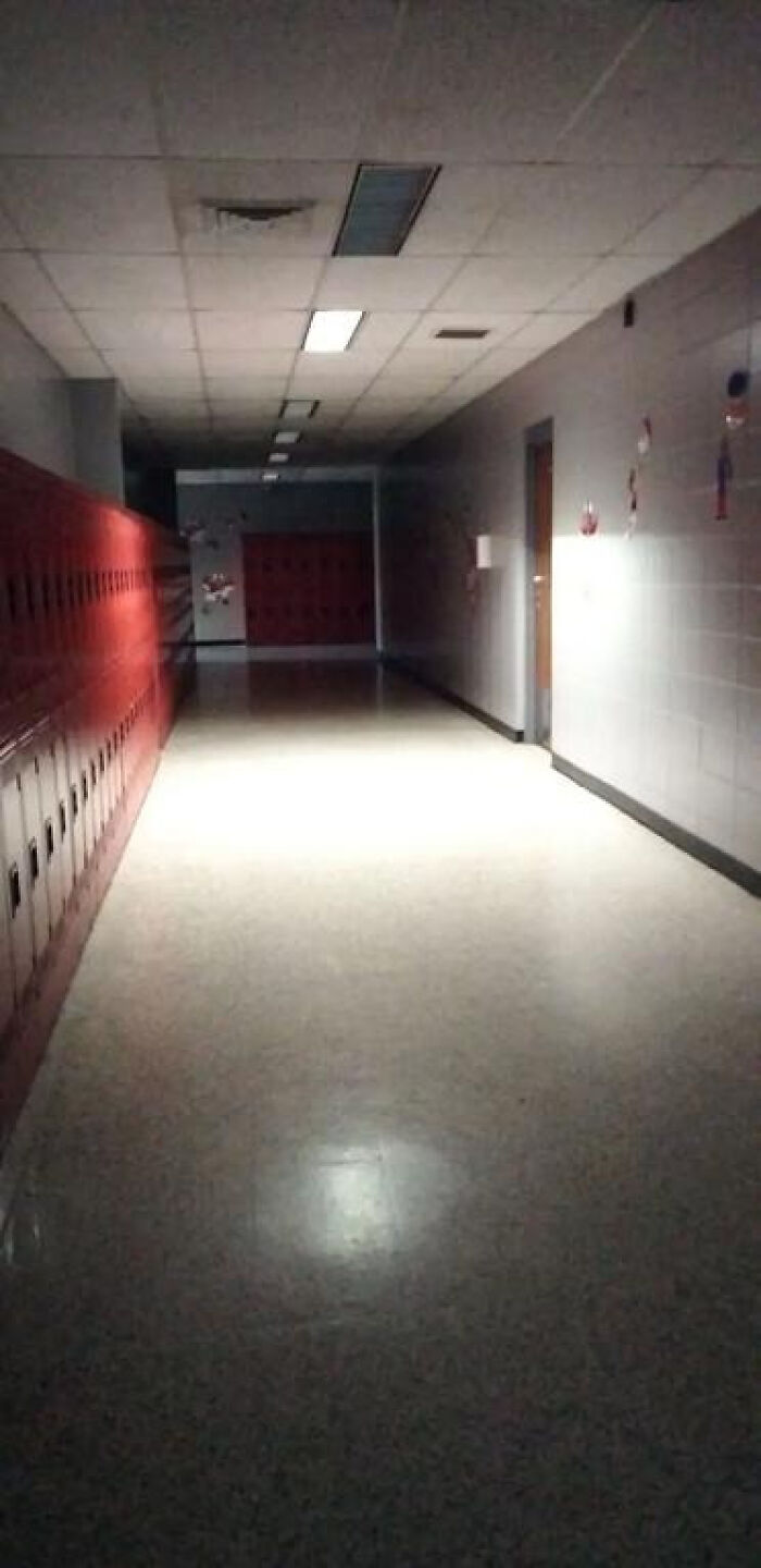 A long, dimly lit school hallway with red lockers, an unsettling and haunting liminal space.