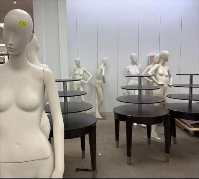 A haunting liminal space with numerous mannequins standing amidst empty display tables in a deserted store.