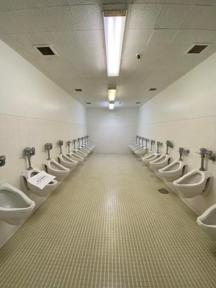 A long, sterile restroom with rows of urinals, a prime example of haunting liminal spaces.