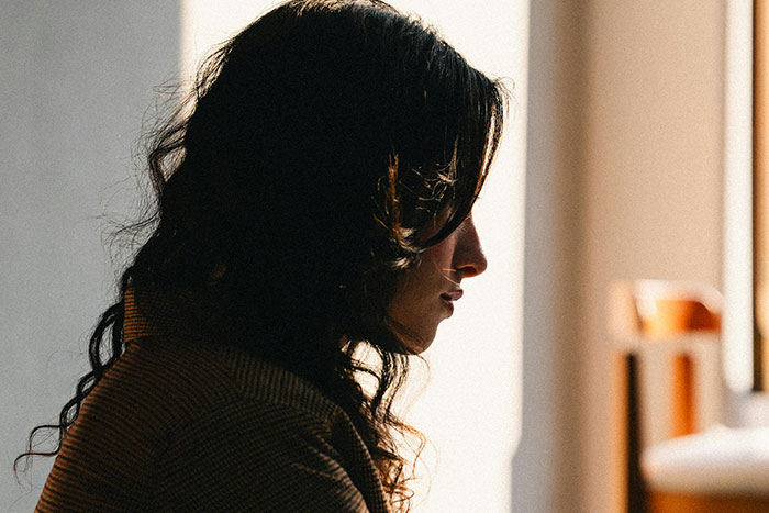 Woman in profile sitting thoughtfully in dim light, appearing troubled