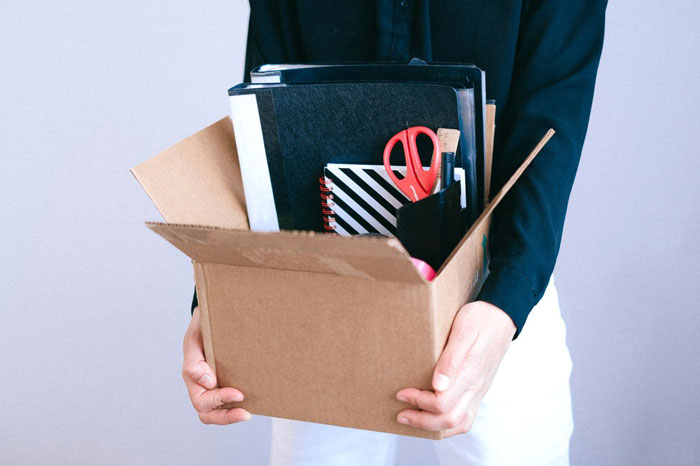 A woman holds a box of her belongings, symbolizing her job might be on the line due to her messy hair.