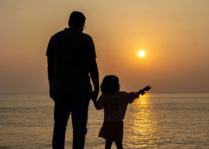 Silhouette of father and child at sunset by ocean reflecting wild secrets of family