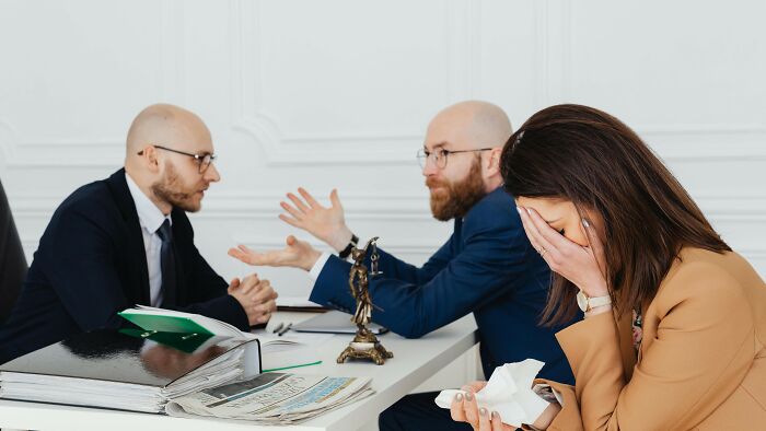 Two men discussing seriously while a woman covers her face in distress