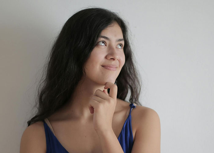 Young woman looking up thoughtfully with hand on chin