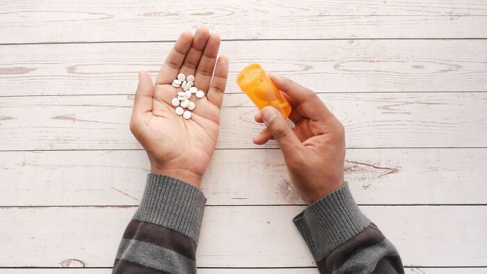 Person holding white pills and orange prescription bottle on table