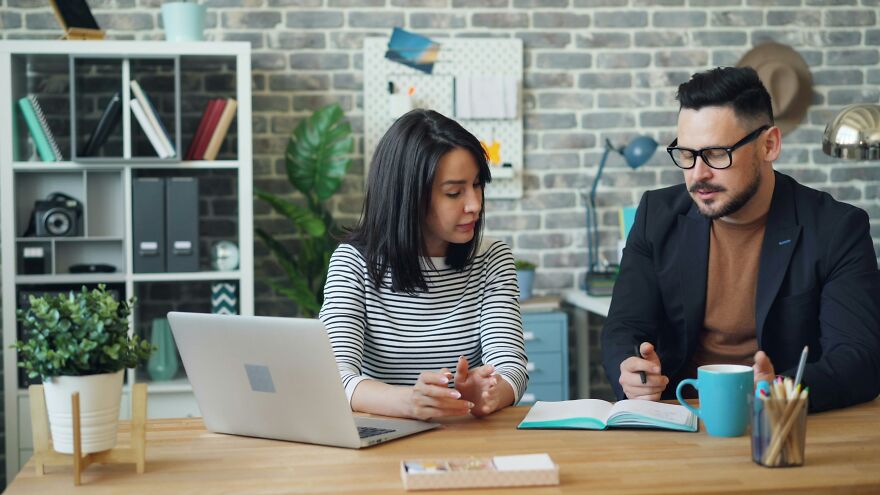 Couple having serious conversation in home office setting with laptop and books