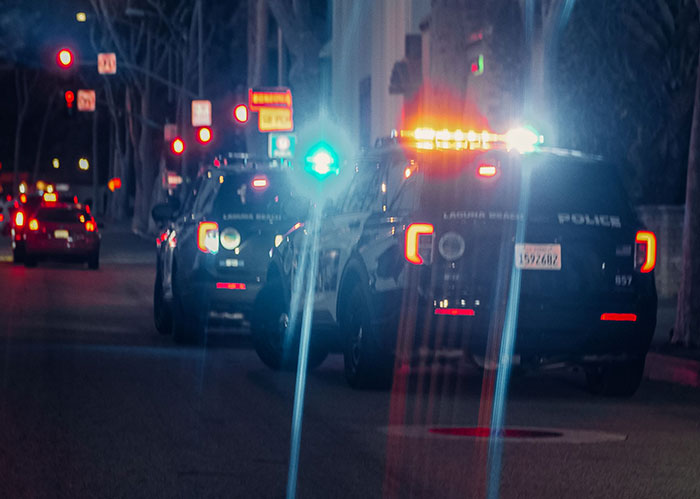 Police cars with flashing lights on a street at night, symbolizing the consequences for popular kids who peaked in high school.