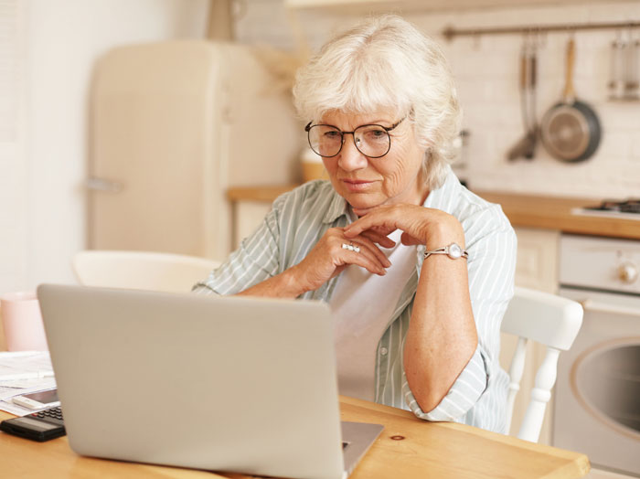 An elderly woman with glasses intently looking at her laptop, contemplating the heartwarming and heartbreaking things on late parents' phones.