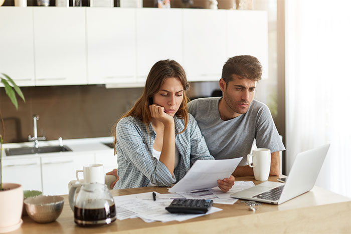 Couple reviewing wedding costs and budget with worried expressions at kitchen table