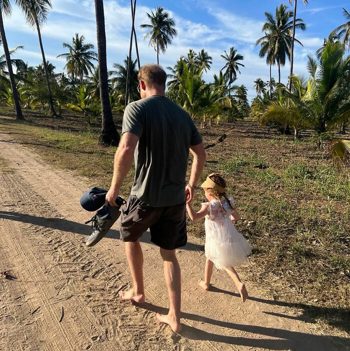Man and child walking barefoot on dirt path with palm trees