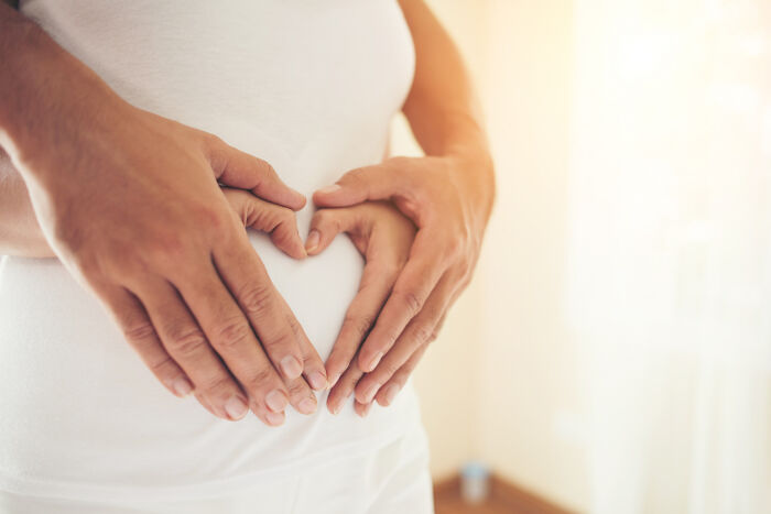 Hands forming heart shape on pregnant belly representing human body pregnancy