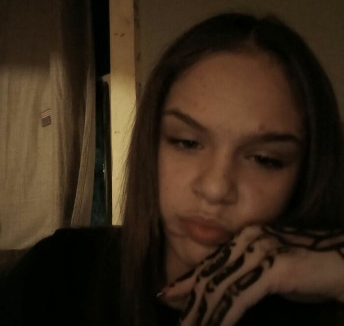 A girl with long brown hair looks down, making a pouting face. She has designs on her hand, a victim of a social media challenge.