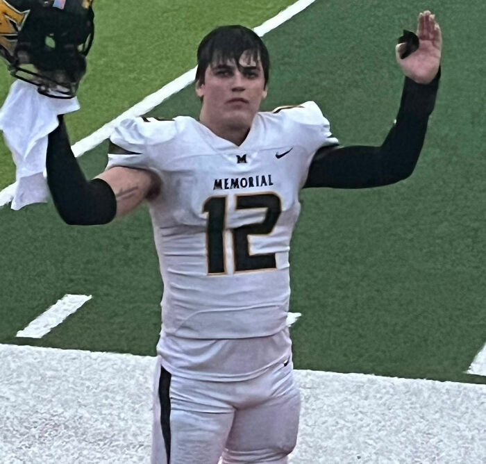 Young football player wearing Memorial jersey number 12 raising arms on field