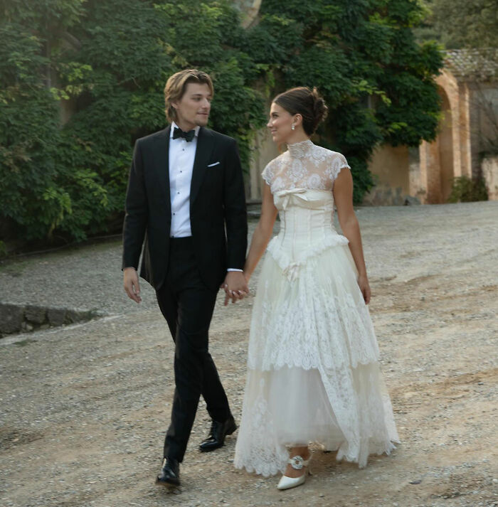 Jake Bongiovi and Millie Bobby Brown holding hands in wedding attire outdoors