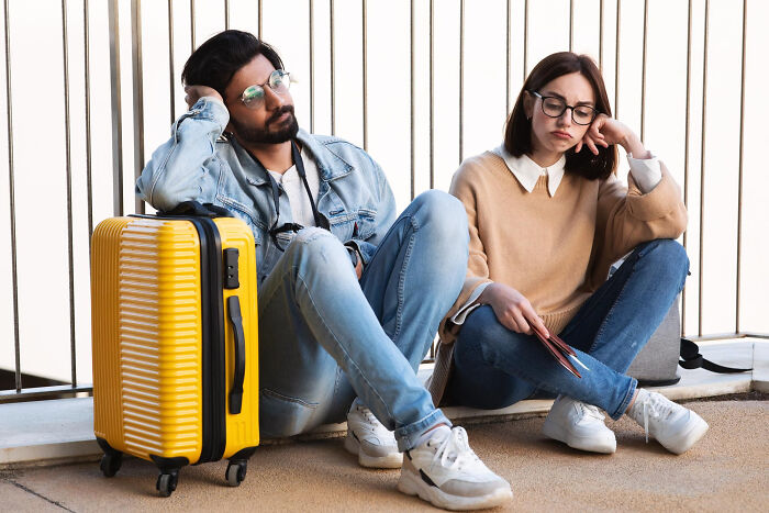 Unhappy couple sitting on ground with luggage, symbolizing unhinged breakup excuses