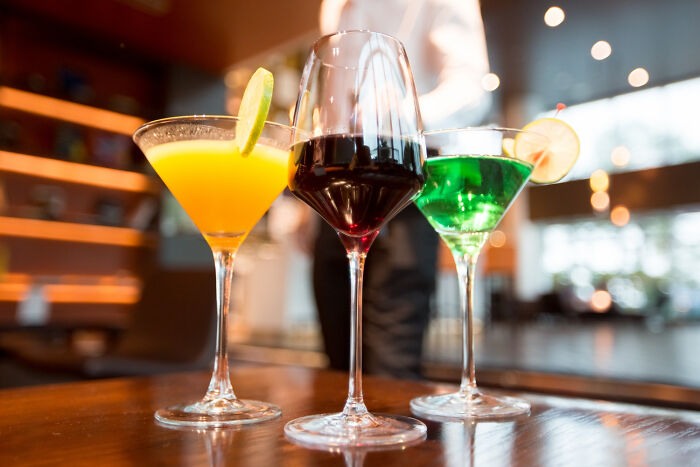 Three colorful cocktails a bright yellow, deep red, and vibrant green sit on a bar, representing disturbing things people learned about their friends.